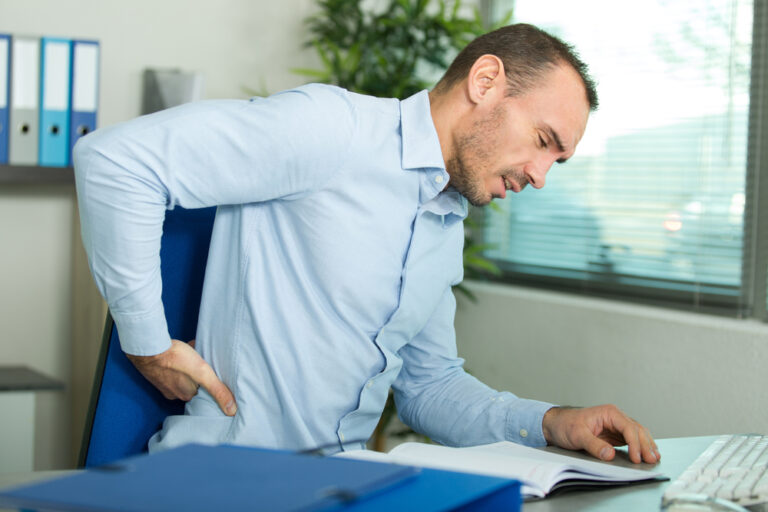 imagem de um homem no escritório de trabalho com a mão nas costas com dorsalgia