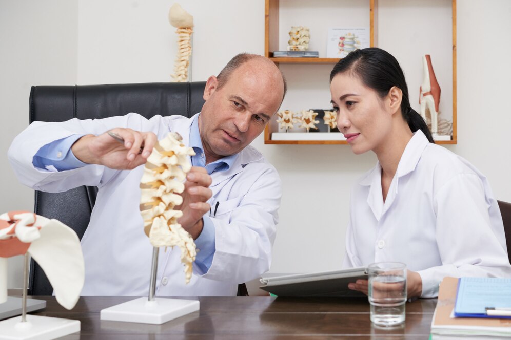 A imagem mostra um médico especialista conversando com outra pessoa sobre como funciona uma parte coluna vertebral.